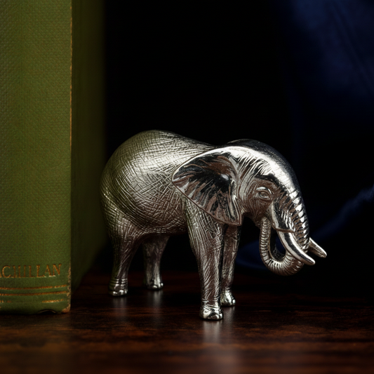 Silver elephant figurine on a dark surface with books in the background